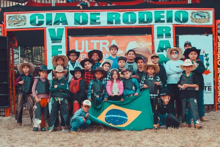Grupo de crianças com chapéus de cowboy segurando a bandeira do Brasil na arena